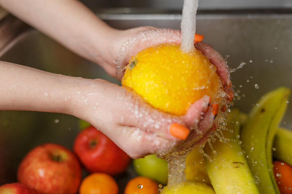 Mãos de uma mulher lavando frutas e legumes na cozinha
