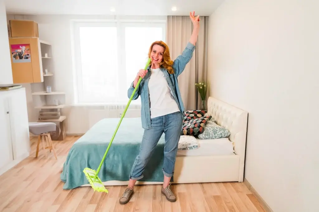 Mulher com vassoura na mão mostrando como limpar o quarto